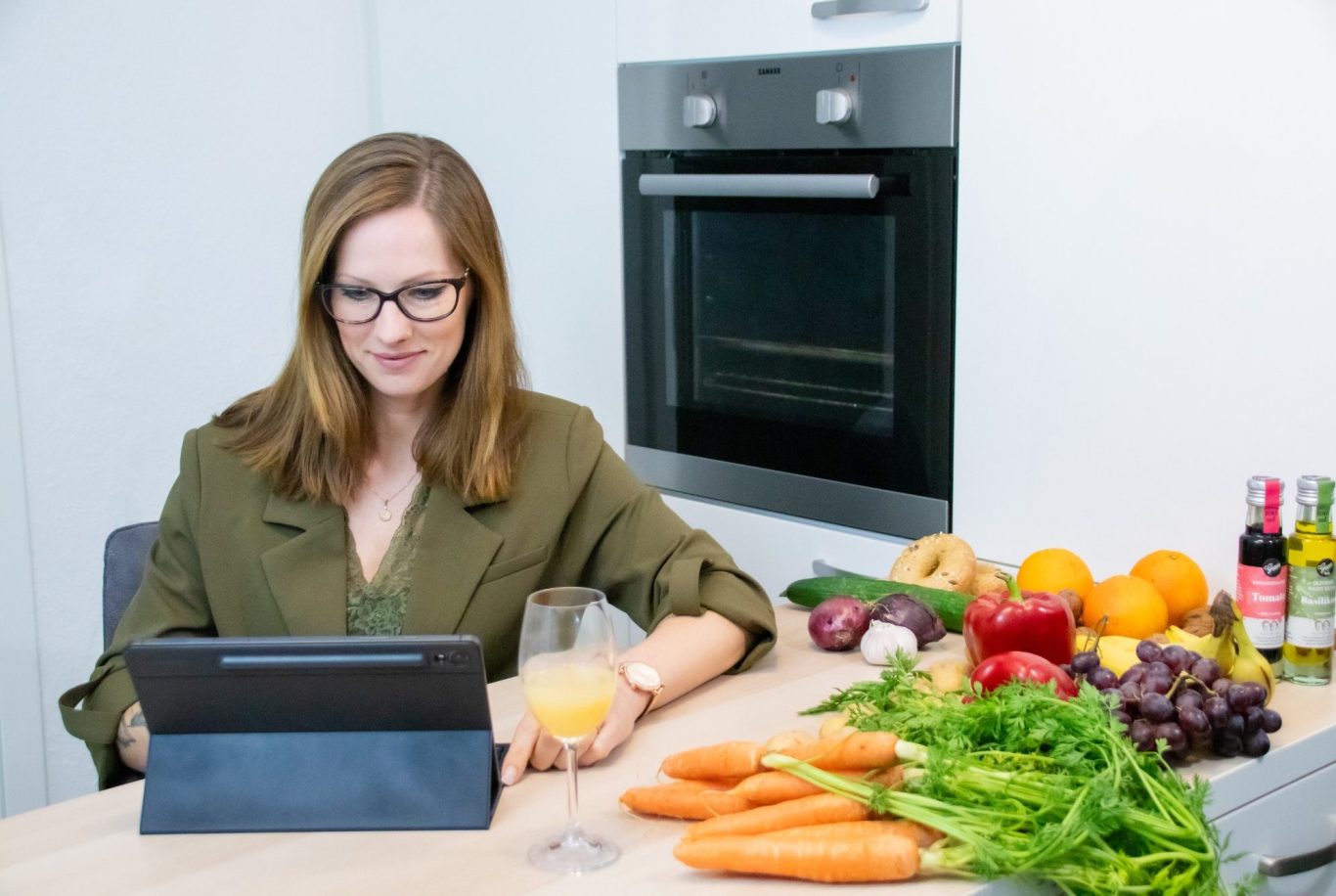 Betriebliche Gesundheitsförderung Frau mit Tablet an einem Tisch, umgeben von frischem Gemüse und einem Getränk.
