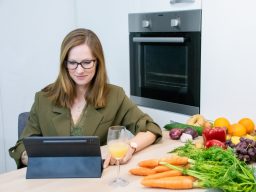 Ernährungsberatung Frau mit Tablet am Tisch, umgeben von frischem Gemüse und einem Getränk.