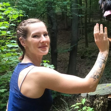 Sport im Wald Frau mit geflochtenem Haar, die im Wald einem Hund zuwinkt.