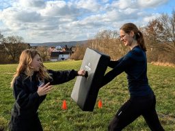 Training mit Kindern Zwei Frauen trainieren im Freien, eine schlägt auf ein Trainingsschild.