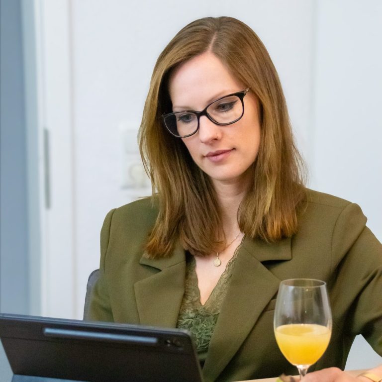 Management Hände tippen auf einer Laptop-Tastatur, daneben Notizbuch und Pflanze auf einem Tisch.